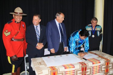 Peerless Trout First Nation Chief James Alook signs as (from left) RCMP Sgt. Ral