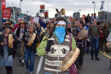 A masked woman leads a crowd of several thousand people marching across the Camb